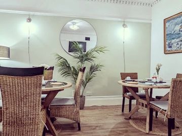 Cozy dining area with wicker chairs and wooden tables in a softly lit room.