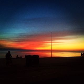Vibrant sunset over calm waters with silhouetted figures and a cyclist.