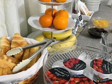 A breakfast spread with croissants, fruits, strawberry yogurt, and jams.