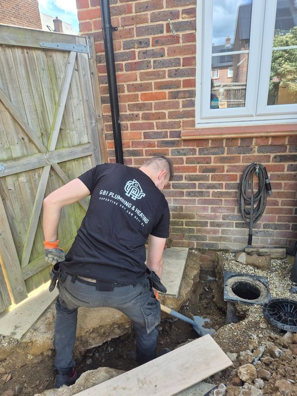 Worker digging a hole near a house.
