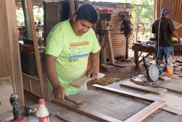 A man works on woodcraft in a workshop, wearing a bright green NASA t-shirt.