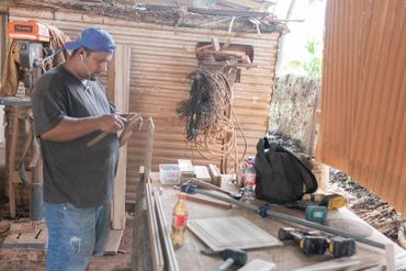 Man sanding wood in a rustic workshop filled with tools and materials.