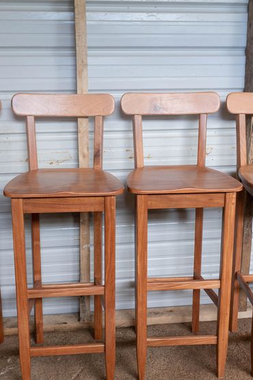 Two wooden bar stools with backrests against a metal wall.