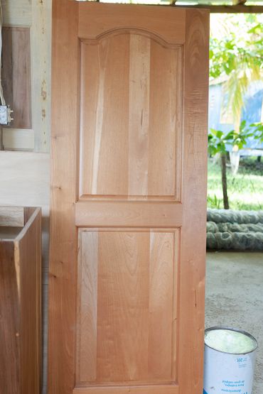 A wooden door panel leaning against a wall near a paint can outdoors.