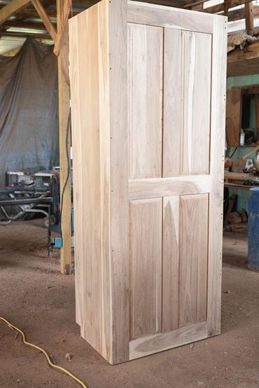 Unfinished wooden cabinet standing in a workshop.
