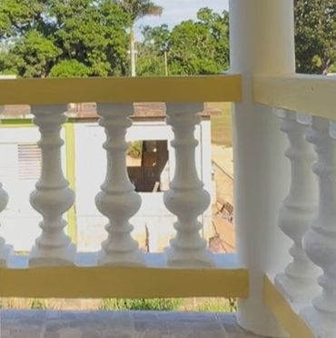 White decorative balustrade on a porch with trees in the background.