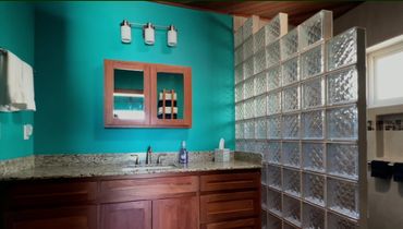Bathroom with turquoise walls, wooden cabinets, and glass block shower divider.