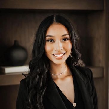Confident woman with long black hair smiling in a black outfit indoors.