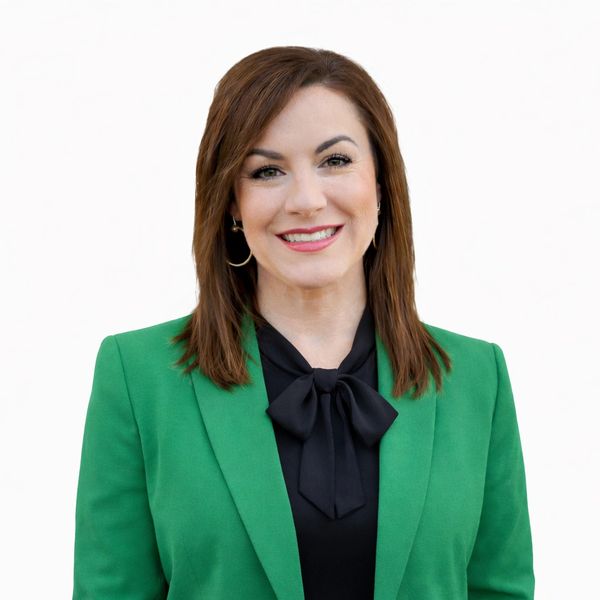 Professional woman wearing a green blazer and black blouse with a bow, smiling at the camera.