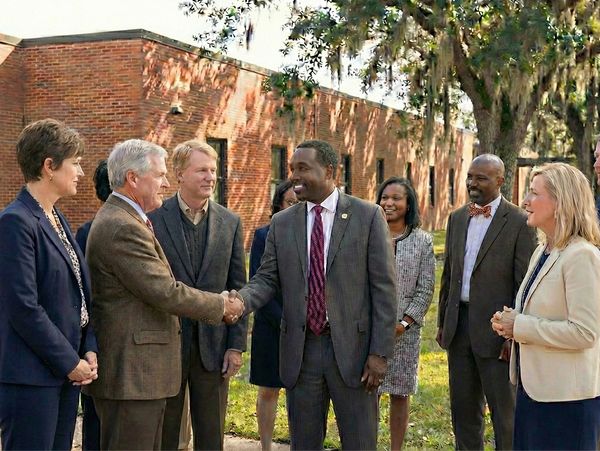 A group of professionals shaking hands and smiling outdoors near a brick building.