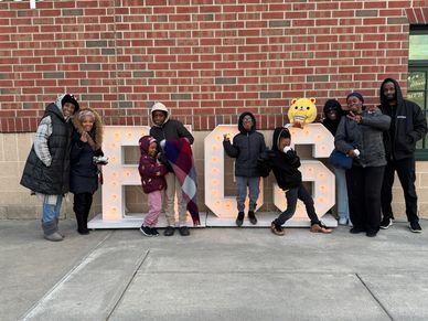 Group of people posing by lighted letters 'BGS' outdoors.