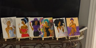 Six colorful paintings of women with natural hair on easels.