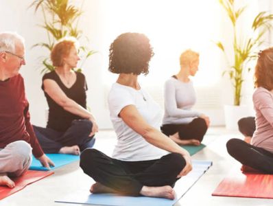 A group of people practicing yoga, sitting down on yoga mats in a seated twist pose.