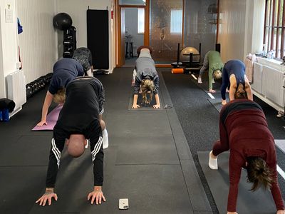 A group of people practicing yoga in a studio, in downward facing dog pose.