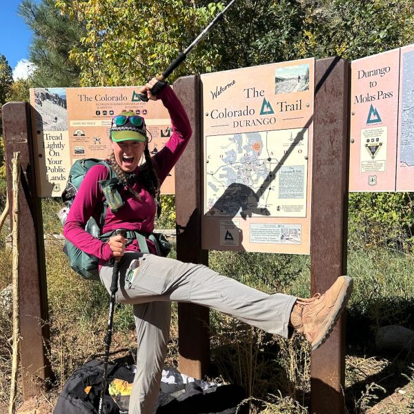 Excited hiker poses cheerfully by Colorado Trail sign.