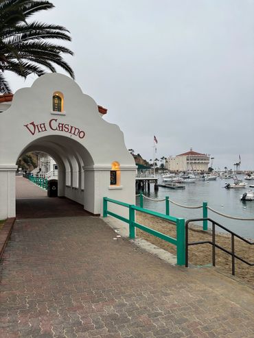 Entrance archway to Via Casino by the waterfront with boats and a large round building in the background.