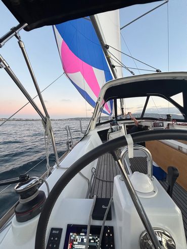 View from a sailboat cockpit with colorful sails and calm waters at dusk.