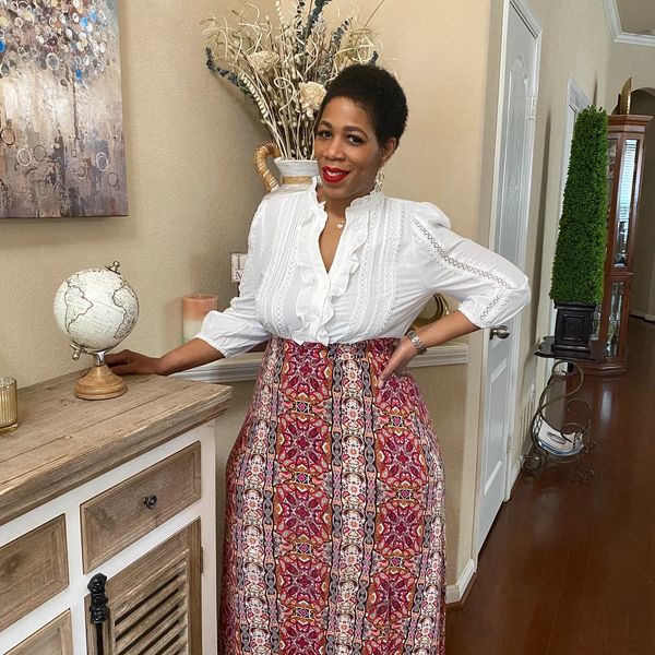 Woman posing indoors wearing a white blouse and patterned skirt.