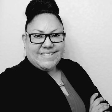 Confident woman smiling, wearing glasses and business attire in a black and white photo.