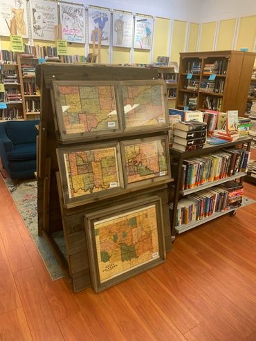 Vintage framed maps displayed on a wooden stand in a cozy bookstore.