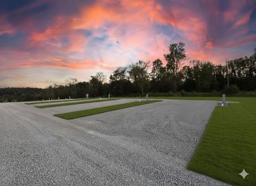 Empty gravel parking area with grass dividers under a colorful sunset sky.
