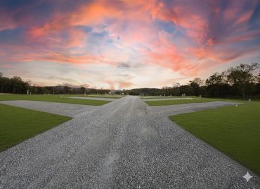 A gravel road intersection with vivid sunset sky and green grass fields.