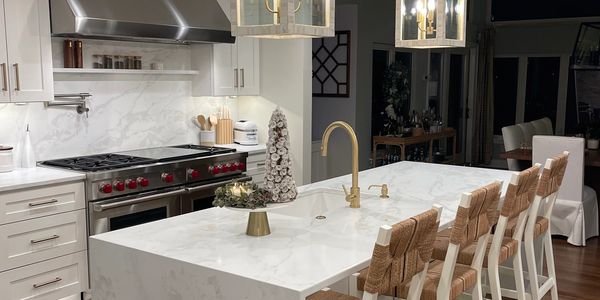 Modern kitchen with marble island, gold fixtures, and woven bar stools.