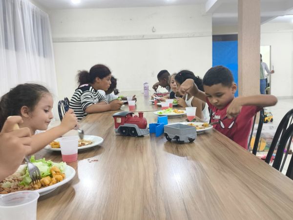 Crianças almoçando juntas em uma mesa com brinquedos de trem.