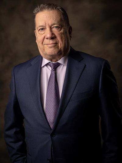 Portrait of an older man in a dark suit and patterned tie.