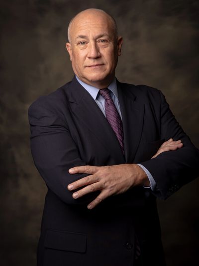 Confident bald man in a dark suit with arms crossed.
