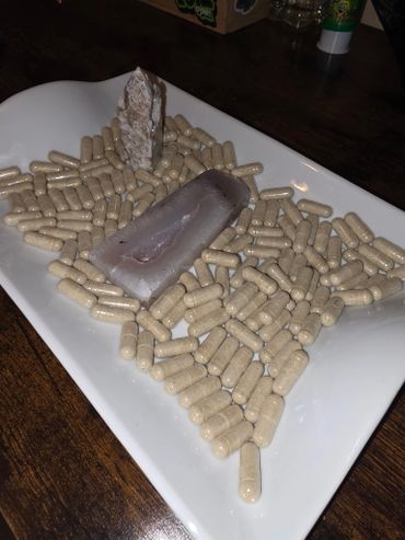 A white plate filled with beige capsules and two crystals on a wooden surface.