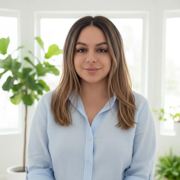 Nurse Ellen, dressed in a light blue shirt, sits indoors with a calm and reassuring smile. The scene reflects her role as a Medi-Cal approved doula, offering emotional support during pregnancy and holistic wellness care for expectant families.