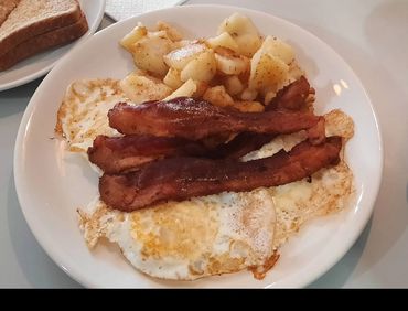 Plate with fried eggs, crispy bacon strips, and seasoned potatoes.