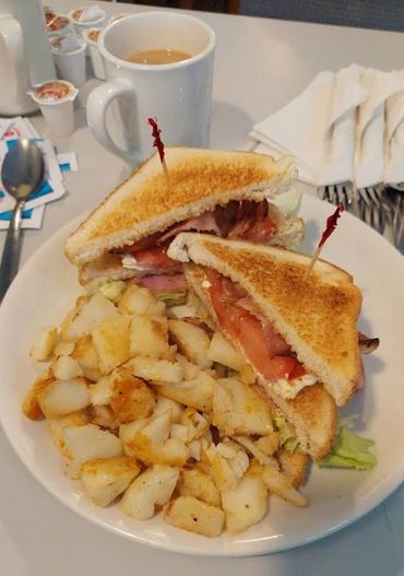 Club sandwich with crispy potatoes and coffee on a white plate.