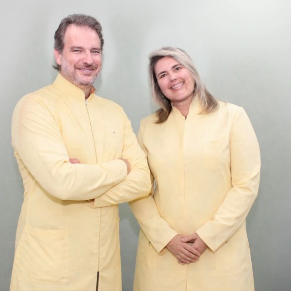 Dois profissionais de jaleco amarelo sorridentes.