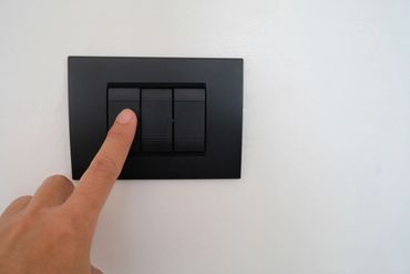 Finger pressing a black light switch on a white wall.