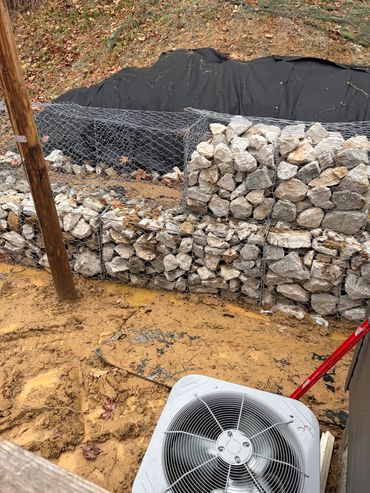 Tiered gabion basket retaining wall built with of stone for erosion control and slope stabilization.