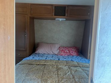Cozy bed with wooden cabinets overhead.