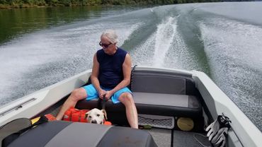 Man in blue shorts and sleeveless shirt with a dog on a boat ride.
