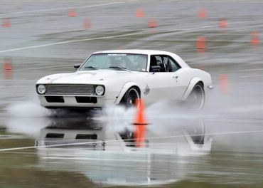 White classic car drifting on a wet track with orange cones.