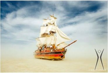 A ship sailing through a desert with sails open.