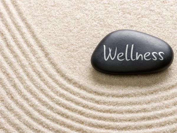 Smooth black stone with Wellness written on it. The stone is sitting on sand that has been combed.
