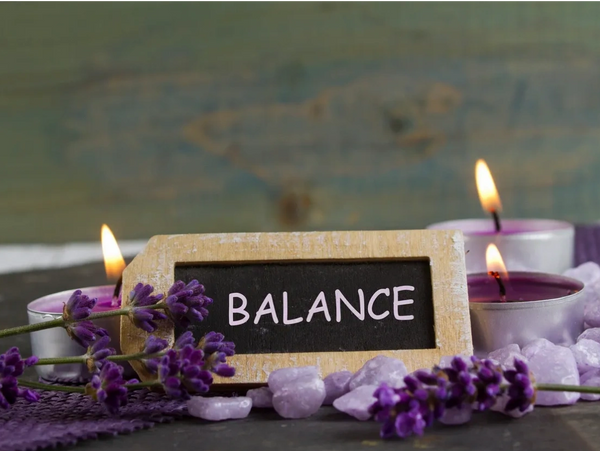 Balance on a sign surrounded by purple candles and lavender flowers.
