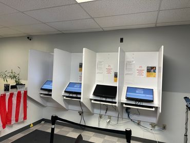 Four voting booths with computer screens in an indoor polling station.