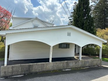 White carport with three arches in front of a house on a sunny day.