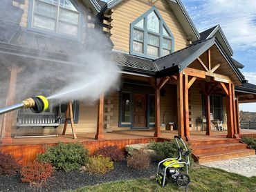 Pressure washing a wooden porch of a house on a sunny day.