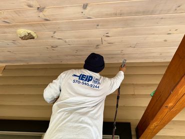 A painter in a white shirt and black beanie spray painting a wooden ceiling.