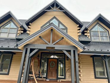 Front entrance of a rustic log cabin house with a porch swing and decorative wreath on door.