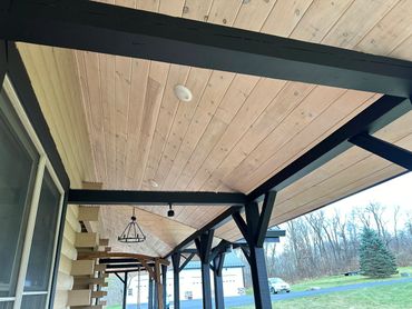 Covered wooden porch ceiling with black beams and light fixtures.