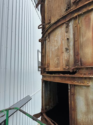 Rusty metal structure with an open section next to a corrugated wall.